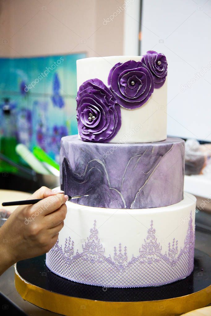 Hand with brush decorating purple wedding cake