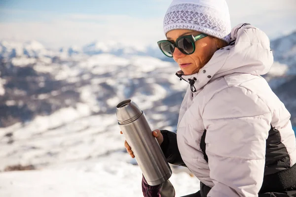 Adult woman with thermos of tea on mount top with spectacular view of snowy mountains on background. Bakuriani, Georgia, mount Kokhta