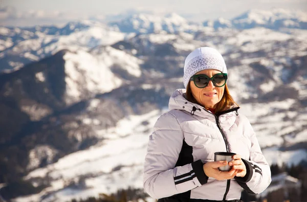 Adult woman with thermos of tea on mount top with spectacular view of snowy mountains on background. Bakuriani, Georgia, mount Kokhta