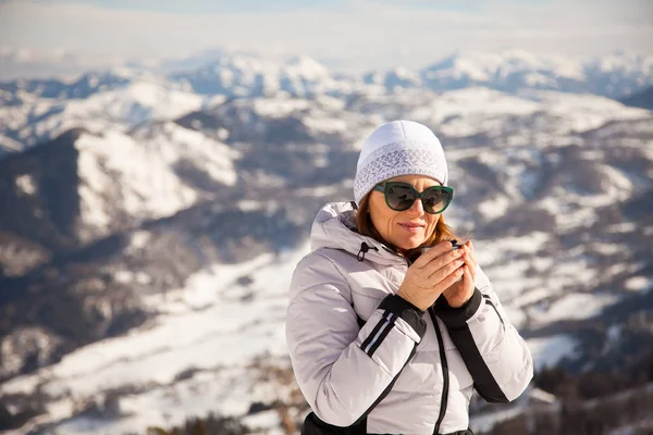 Adult woman with thermos of tea on mount top with spectacular view of snowy mountains on background. Bakuriani, Georgia, mount Kokhta