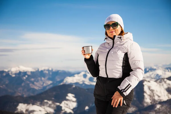 Взрослая женщина с термосом на вершине горы с захватывающим видом на снежные горы на заднем плане — стоковое фото