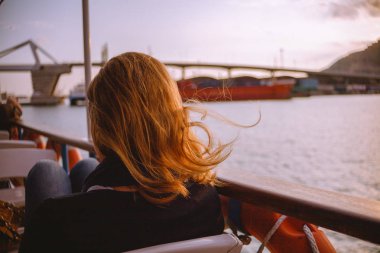 Arkadan genç kadın oturma modern turistik tekne korkuluk rüzgarlı akşam gezisi sırasında yakın görünüşü