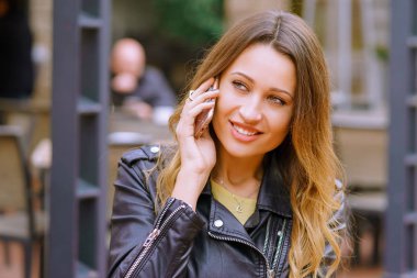 Arka plan açık kafe ve smartphone konuşmayı gülümseyen ve uzak otururken arıyorum güzel genç bayan bulanık