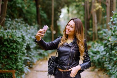 Bir parkta ağaçların arasında tam bir selfie alarak mutlu kız