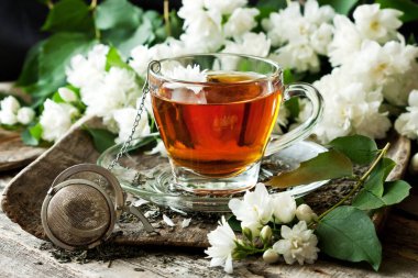 Çay bardağı ile ahşap arka plan üzerinde Yasemin çiçekleri. Seçici odak, sığ derinlik-in tarla