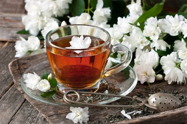 Çay bardağı ile ahşap arka plan üzerinde Yasemin çiçekleri. Seçici odak, sığ derinlik-in tarla