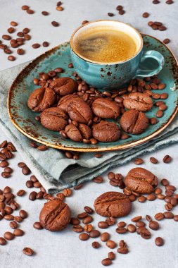 Kahve kupalı kompozisyon, kahve şeklindeki kurabiyeler, gri arka planda kahve çekirdekleri.