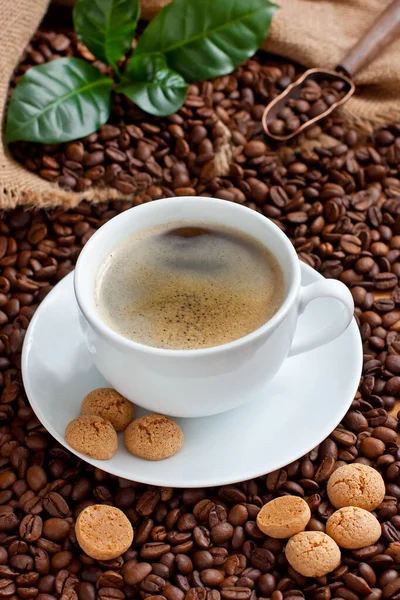 Composition with coffee mug, almond cookies, coffee beans in burlap bag on dark background