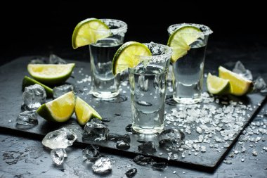 Sulu limon dilimli tekila shot ve siyah arkaplanda tuz.