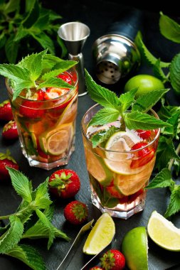 Naneli limon ferahlatıcı kokteyl mojito çilekli ve buzlu siyah arka planda.
