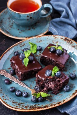 Yaban mersinli çikolatalı kek ve koyu beton arka planda çaydanlıklı çay fincanı.