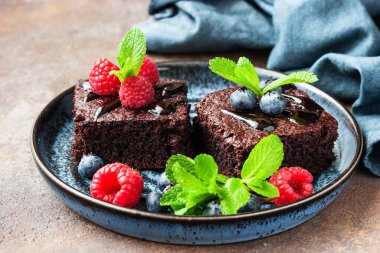 Böğürtlen ve nane yapraklarıyla süslenmiş çikolatalı brovniler renk arkaplanında, seçici odak alan derinliği sığ