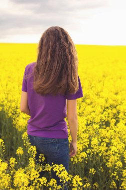 Sarı tarla çiçeklerinin arka planında genç bir kız.