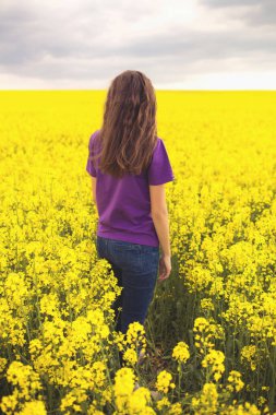 Sarı tarla çiçeklerinin arka planında genç bir kız.