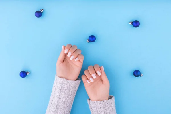 Hermosa mano de mujer joven con manicura sobre fondo azul con bolas de Navidad . — Foto de Stock