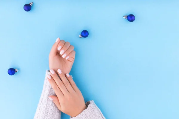 Hermosa mano de mujer joven con manicura sobre fondo azul con bolas de Navidad . — Foto de Stock