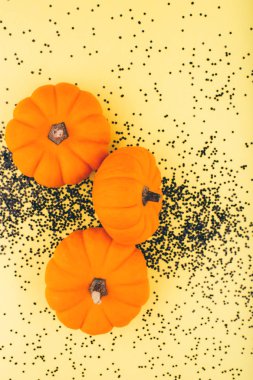 Sarı arka planda siyah konfetiyle Cadılar Bayramı balkabakları. 