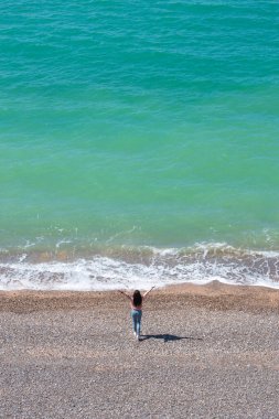 Kız güzel mavi bir denizin kıyısında duruyor ve uzaklığa bakıyor. Yukarıdan manzara. Güzel manzara..