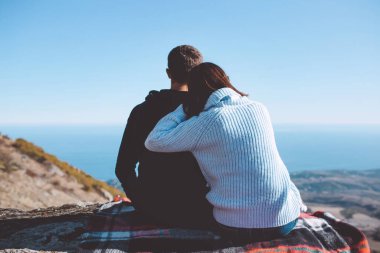 Sırt çantalı sevgi dolu bir çift dağlarda bir kayanın üzerinde oturur ve doğanın tadını çıkarır. Doğa geçmişi. Yolculuk. Dağlara bir yolculuk..