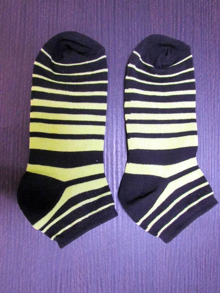 Striped baby socks, in black and yellow stripes, lie on a purple table