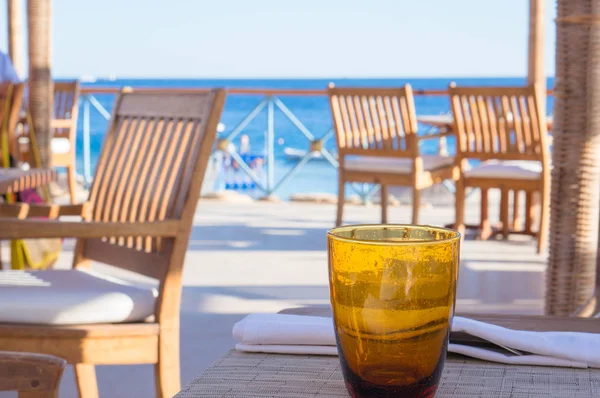 An empty orange glass standing on table at beach cafe with sea view