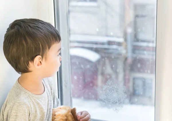 Μικρό αγόρι βλέποντας χιονισμένο καιρό μέσα από το παράθυρο Εικόνα Αρχείου