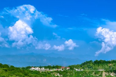 Mavi bulutlu beyaz gökyüzü, sis ve evleri ile kaplı dağ eteklerindeki doğal görünümü