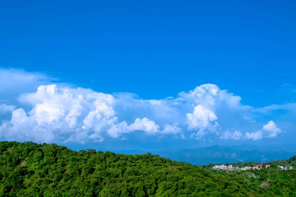 Mavi bulutlu beyaz gökyüzü, sis ve evleri ile kaplı dağ eteklerindeki doğal görünümü
