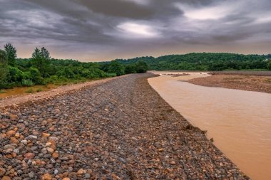 Gabion, Kafesler Erozyon kontrol etmek için Riverbank yerleştirilen Kayalar ile dolu, Karanlık Gökyüzü ve Nehir kirli su Arka Plan, yağmur sonrası yağmur mevsimmanzara.