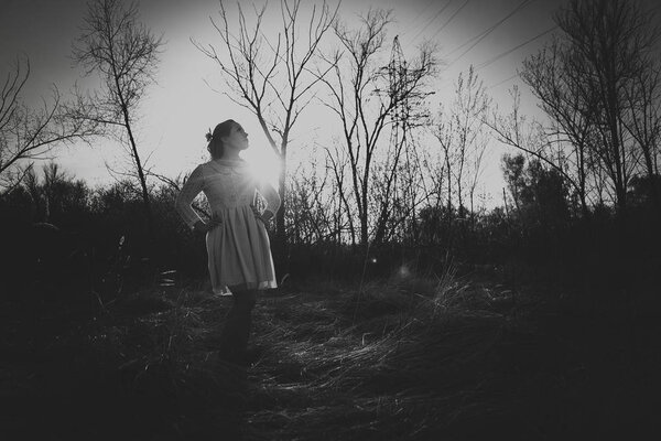 Blackwhite photo girl standing in a field on a sunset background.