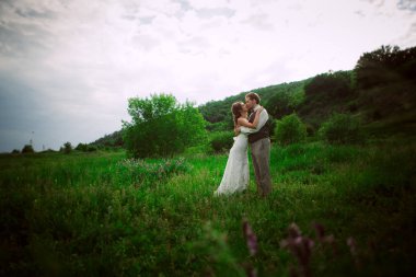 Gelin ve damat dağ ve çim arka plan üzerinde durmak.