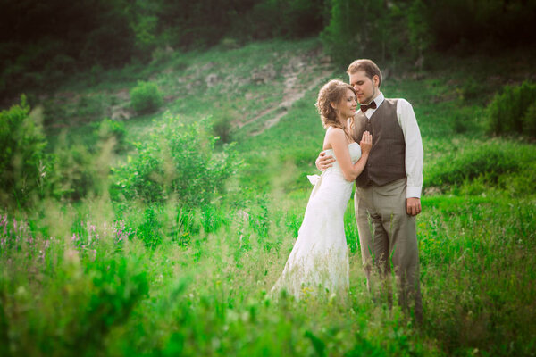 Bride and groom stand on the background of the mountain and grass.