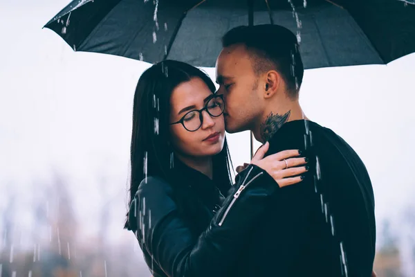 young couple standing under a dark umbrella.