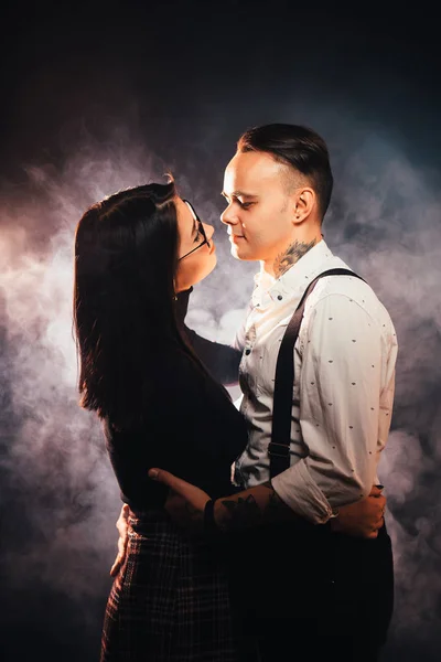 Couple in fashionable clothes on a dark smoky background.