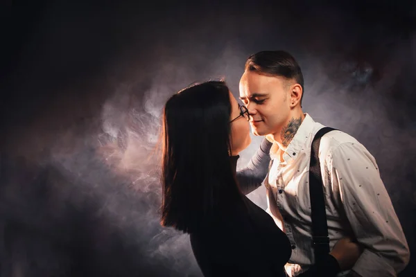 Couple in fashionable clothes on a dark smoky background.