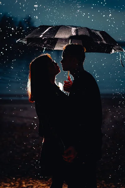 Genç erkek ve kadın bir şemsiye ve yağmur altında