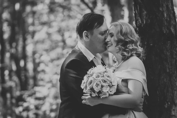 Svartvit foto bruden och brudgummen kyssa på bakgrunden av träd och skog — Stockfoto