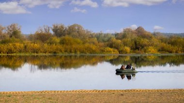 Nehri kıyısında, hangi iki balıkçı ile tekne yüzen sarı yapraklarla kaplı ağaçlar büyümeye. Sunny sonbahar günü.