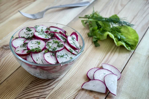 On the table, chopped salad radish in a glass bowl and arugula grass.