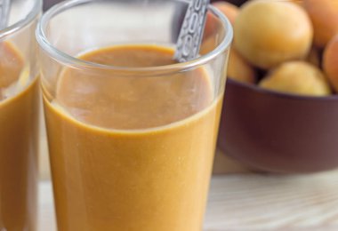 İki cam bardak ile peçeteye masada kayısı güler yüzlü. Yanındaki kayısı cam vazoda.