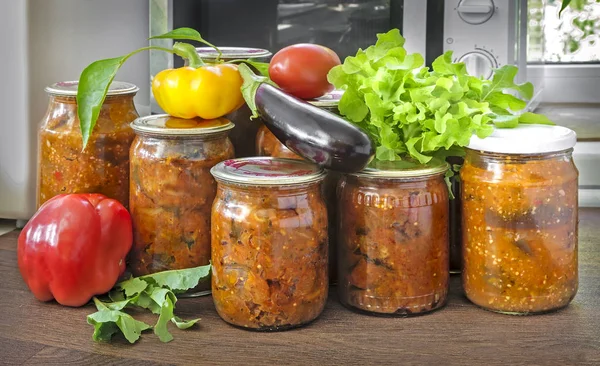 Çeşitli sebze mühürlü metal kapakları ile cam kavanozlara korunur: Patlıcan, biber, domates, soğan. Taze sebze ve yeşil salata yakındadır.