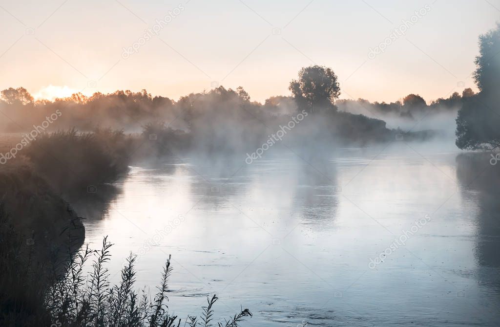 Beautiful calm river with the mist over the surface of the water at dawn by the light of the rising sun.