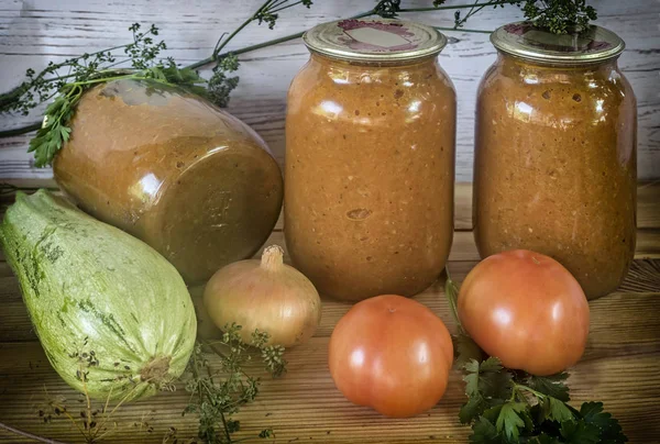 Home preservation of vegetables: glass jars with zucchini caviar with onions, tomatoes, garlic, herbs. With airtight cover made of metal.