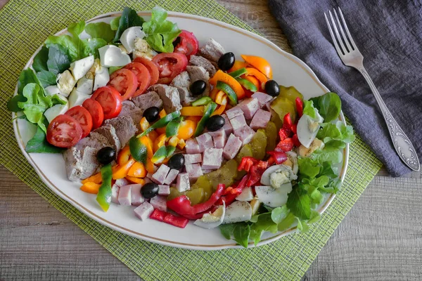 A popular dish of American cuisine - Cobb salad, consisting of greens, eggs, tomatoes, cheese, meat products, stacked in rows on a wide dish and poured sauce.