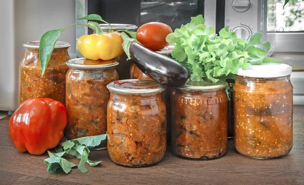 Çeşitli sebze mühürlü metal kapakları ile cam kavanozlara korunur: Patlıcan, biber, domates, soğan. Taze sebze ve yeşil salata yakındadır.