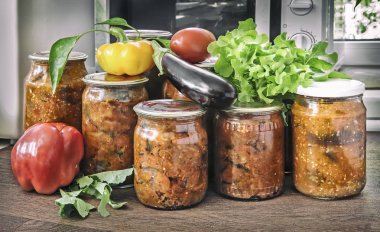 Çeşitli sebze mühürlü metal kapakları ile cam kavanozlara korunur: Patlıcan, biber, domates, soğan. Taze sebze ve yeşil salata yakındadır.