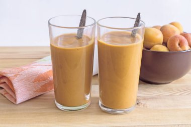 İki cam bardak ile peçeteye masada kayısı güler yüzlü. Yanındaki kayısı cam vazoda.