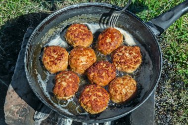 Büyük bir tavada kamp ateşi üzerinde leziz köftesi tavada kızartılmış.