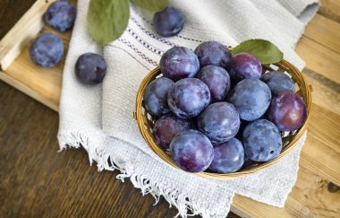 Olgun büyük erik ile dolu bir peçete hasır sepet üzerinde masaya.