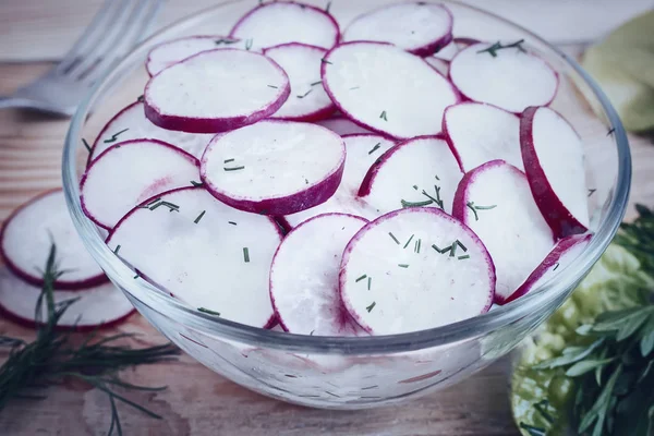 On the table, chopped salad radish in a glass bowl and arugula grass.